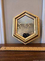 Front view of small hexagonal gold vein mirror against wall with ruler for scale