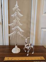 Clear acrylic decorative tree with white frosted base and icicle style drips on branches, placed on wooden surface with measuring ruler nearby for scale.