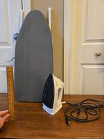 Side view of the small tabletop ironing board with gray fabric cover and Sunbeam steam iron placed in front, cord coiled, a ruler measuring approximately 12 inches is held vertically indicating the height of the board's standing position.