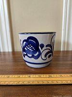 Front view of small ceramic plant pot with blue floral decoration and included ruler for scale.