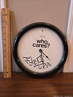 Full view of clock with ruler showing size, clock face with 'Who cares?' phrase and jumbled numbers.
