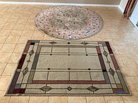 Photo of two rugs on tiled floor. Foreground shows rectangular rug with geometric design, background shows round rug with floral medallion.