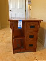 Side view of wooden Arts & Crafts style console end table showing three drawers with metal hardware, two open shelves, and a magazine rack area with visible wear and missing hardware.