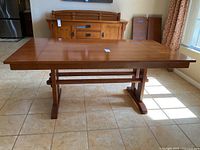Front angle view of the extended wooden dining table showing the trestle base and smooth top surface in natural light.