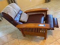 Side view of reclining chair showing wooden slatted armrests, dark burgundy leather cushions, and extended footrest in reclined position with pillow and fabric headrest cover.