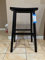 Front view of black solid wood bar stool showing square seat, legs, footrest and tags.