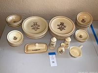 Top-down photo showing all dinnerware and accessory pieces arranged in groups by type on a table, showcasing the cream color and brown floral pattern.