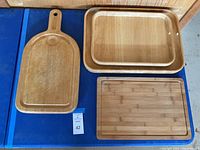 All wooden cutting boards and trays displayed flat on a blue surface showing their shapes, size differences, and wood finish.