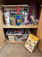 Photo of crafting supplies inside cabinet showing spray adhesive, twine, liquid glue, electric tool, wire baskets with materials, and yellow craft box