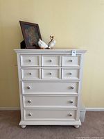 Full view of the white dresser with decorative items on top against a beige wall