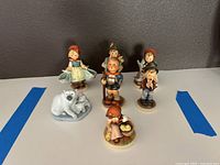 Front view of six Hummel figurines and one Goebel polar bear figurine grouped together on a table