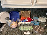 Overview of the kitchen items on a counter showing a mix of glass bottles, jars, plastic containers, bakeware, and accessories