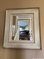 Frontal view of large rectangular wall mirror with textured, light-colored frame hanging on a beige wall.