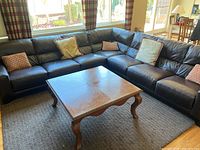 Overall view of dark brown leather sectional sofa, wood coffee table and gray rug