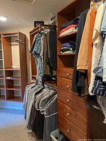 Wide view of wooden closet shelving with men's clothing hanging and folded women's garments.