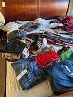 Overview of assorted clothing items on bed including scarves, ties, jackets, tops, and jeans.