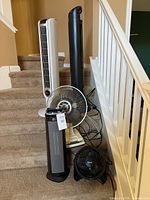 Group photo of five fans and one heater on carpet stairs, showing different models and sizes.