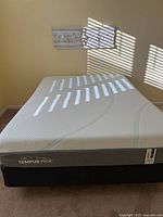 Full top view of white textured Tempur-Pedic mattress on black boxspring on carpeted floor with wall decor above.