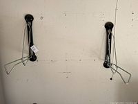 Two black vertical wall-mounted Steadyrack bicycle racks with silver metal hooks, mounted closely side by side on a white wall with visible mounting screws and markings.