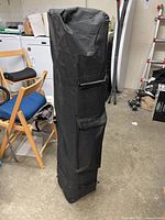 Carrying bag for the canopy, tall and black with side pocket and handle, standing upright