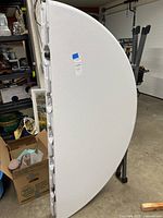 Side view showing white plastic textured folding table top standing vertically folded in garage space.