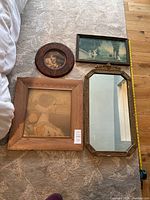 Set of four framed antiques laid out on carpet: rectangular beveled mirror with ornate frame, oval framed portrait print, large square framed print, and smaller rectangular print.