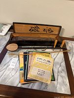 Photo showing the Japanese koto instrument in a wooden box along with Japanese sheet music and the erhu bow.