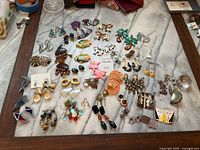 Full collection of assorted earrings displayed on a marble surface showing a wide variety of styles and materials.