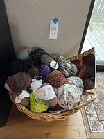 Wicker basket on wooden floor filled with various yarn balls of different colors and textures, alongside the 'Knit Kimono' knitting book.