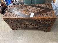 Front perspective of carved wooden chest on concrete floor, showing top and front carvings
