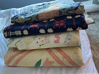 Four antique quilts stacked, showing edges and patterns of each.