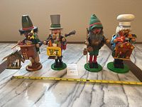 Photo of four wooden smokers including musicians, baker, and hiker on green bases, measuring approx 9 inches tall, arranged on marble surface