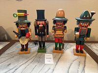 Front view of four vintage nutcracker figures standing on wooden bases, each with different clothing, hats, and accessories, arranged on a marble surface.