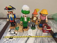 Four vintage wooden nutcracker figurines with a measuring tape showing size roughly 10 to 12 inches.