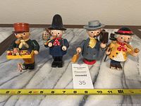 Front view of all four roly poly smoker figurines, showing painted details and approximate height indicated by tape measure beneath (around 5 inches tall)