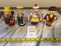 Four roly poly smoker figurines shown upright in a row on marble surface with measuring tape.