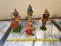 Four vintage wooden smoking figurines displayed on marble surface with measuring tape.