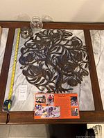 Overall lot displayed on table with measuring tape, showing metal Tree of Life sculpture approximately 21x21 inches, glass bowl, signed metal holder, and informational cards.