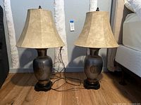 Pair of large vintage Frederick Cooper pewter brutalist table lamps with replacement beige fabric shades, placed on floor against wall.