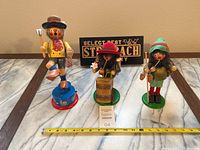 Three vintage Steinbach wooden smoker figurines and a wooden Steinbach sign on marble surface with measuring tape showing size.