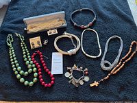 Full lot display showing multiple necklaces of various bead colors and styles, one pair of earrings in box, and a charm bracelet on black cloth background.