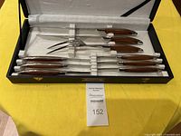 Full view of the set showing 9 pieces including knives and forks, all with wooden handles, arranged inside a black case with cream interior.