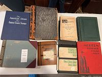Overhead view of nine stamp albums, binders, and one booklet arranged on a table.
