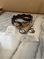 Full belt coiled with earrings alongside business card and MaxSold tag on marble surface