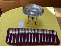 Full view of two-piece footed dish and fifteen spoons on burgundy cloth