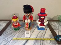 Three Steinbach nutcrackers lined up side by side with measuring tape indicating sizes; includes drummer nutcracker, smaller king nutcracker, and snowman nutcracker.