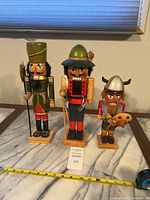 Front view of three wooden nutcracker figures on marble surface with measuring tape at base