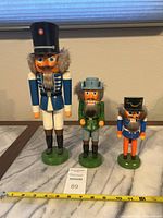 Three nutcrackers shown side by side on table with measuring tape indicating sizes approximately 15, 10, and 8 inches