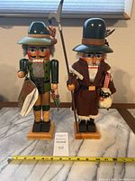 Wide view of two nutcrackers standing side by side on a marble surface showing full height and details with a measuring tape indicating about 15 inches tall