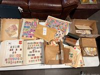 Overview of the entire stamp collection on table including album, envelopes with loose stamps, and multiple boxes containing stamp sheets and envelopes.